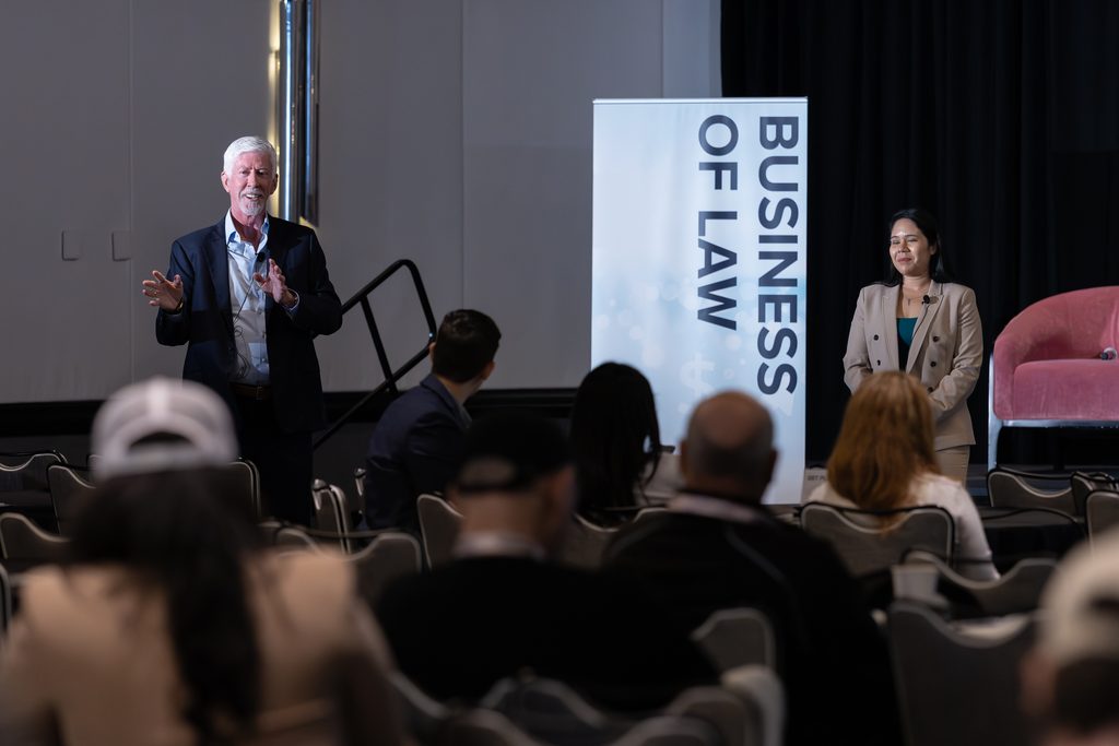 Two speakers addressing attendees during a Business of Law conference session.