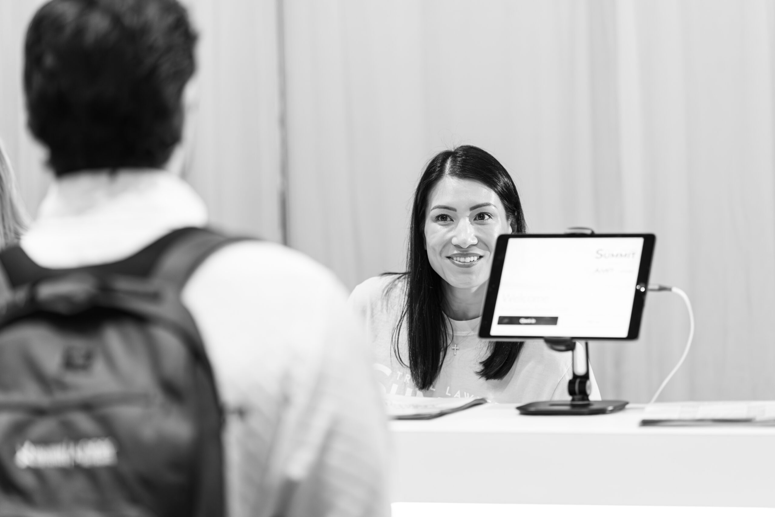Event attendee checking in at a registration desk while a staff member assists them using a tablet.